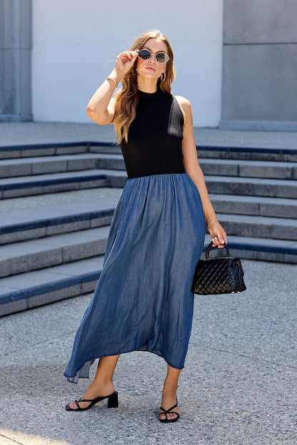 Woman in sunglasses wears the Elan Two Tone Midi Dress - Navy and carries a black quilted handbag outdoors.