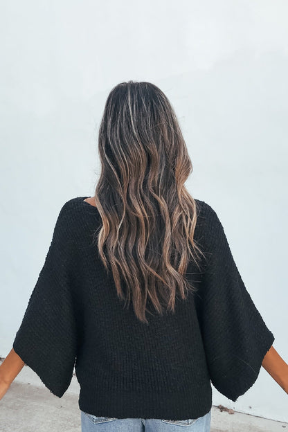 A person with long wavy brown hair wears the Elevated Ribbed Boatneck Sweater in black and blue jeans, facing away against a light background.