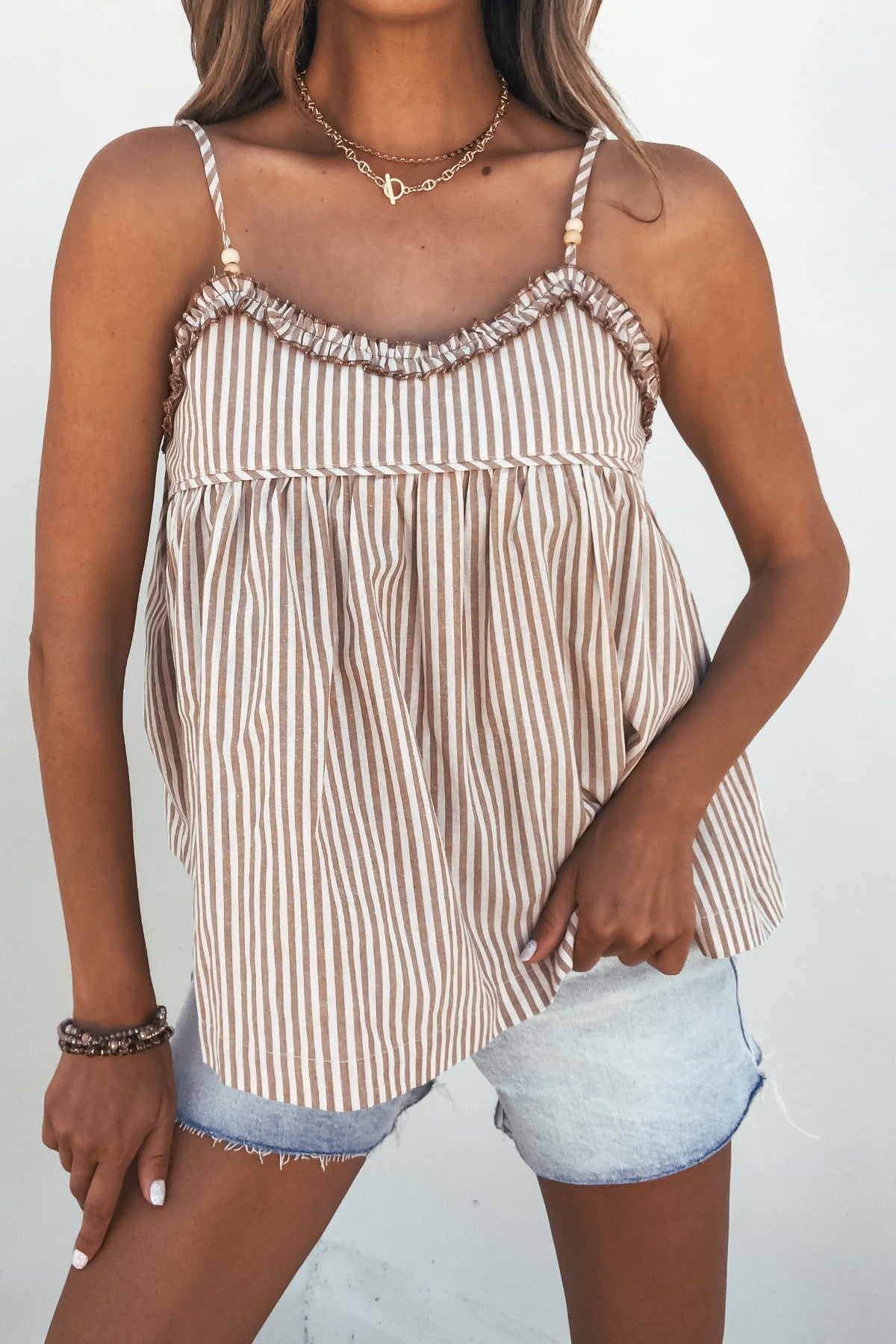 Woman wearing the Ellery Taupe Striped Cami Top with frill detail and light denim shorts, set against a white background.