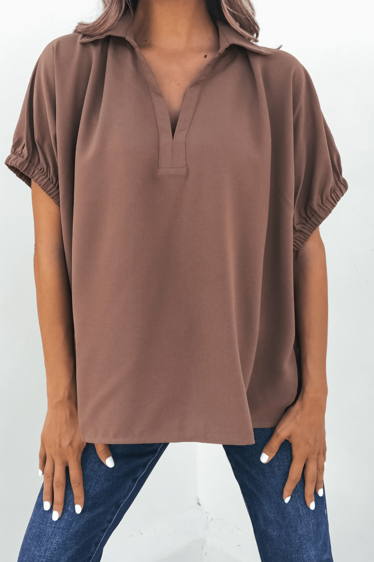 Woman wears the Ellis Camel Split Collared Top with blue jeans, standing against a white background—an autumn essential.