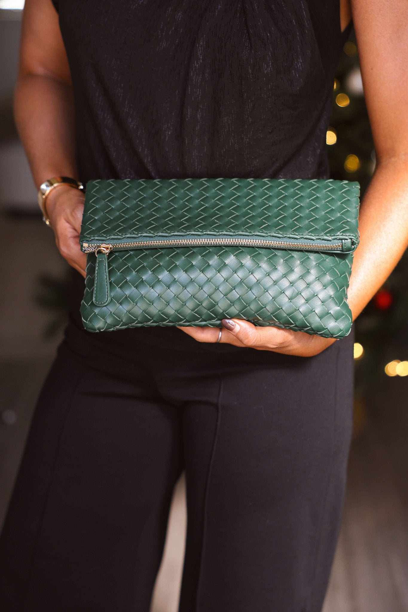 Person holding an Emerald Grace Vegan Leather Clutch with a zipper, paired with a black outfit.