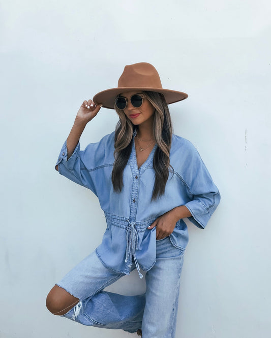 A woman wearing a wide-brim hat, sunglasses, and a light wash blue Waist Tie Half Sleeve Top - Denim.
