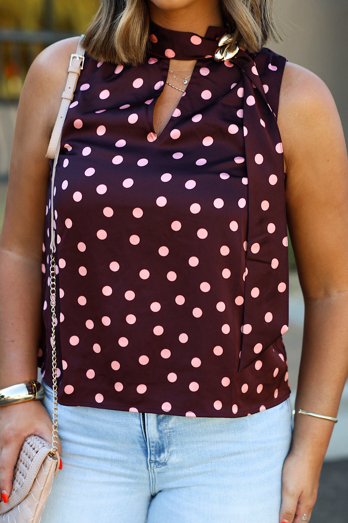 Woman wearing ENTRO T33113 wine polka dot notched neck tank top, light jeans, and holding a beige quilted purse.