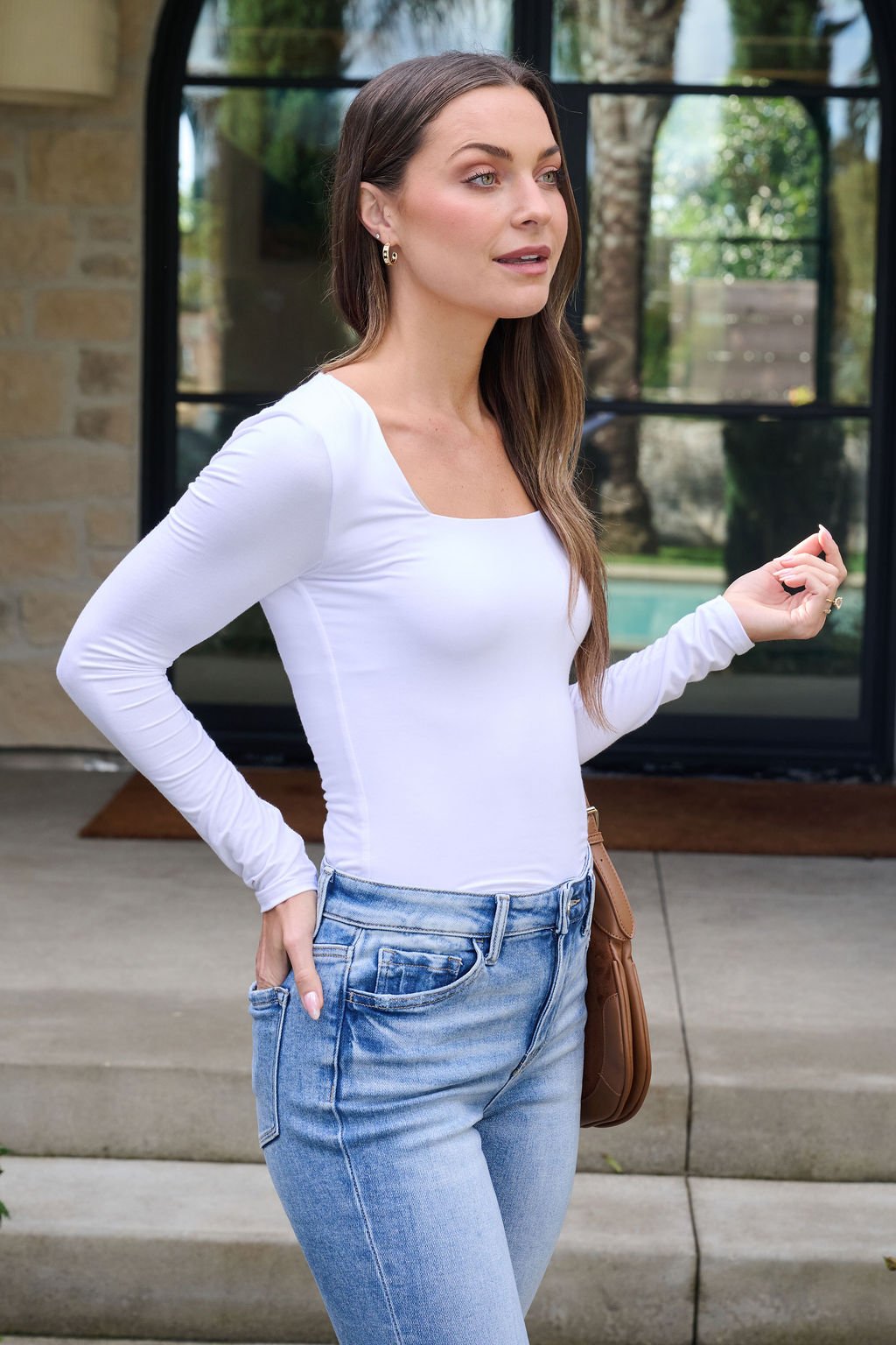 Woman wears the Essential Basic White Square Neck Top with blue jeans, standing outside a building with glass doors and stone walls.