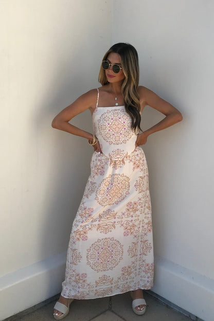 Woman in sunglasses wears the Evelyn Cream Print Maxi Skirt and sandals, standing against a white wall.