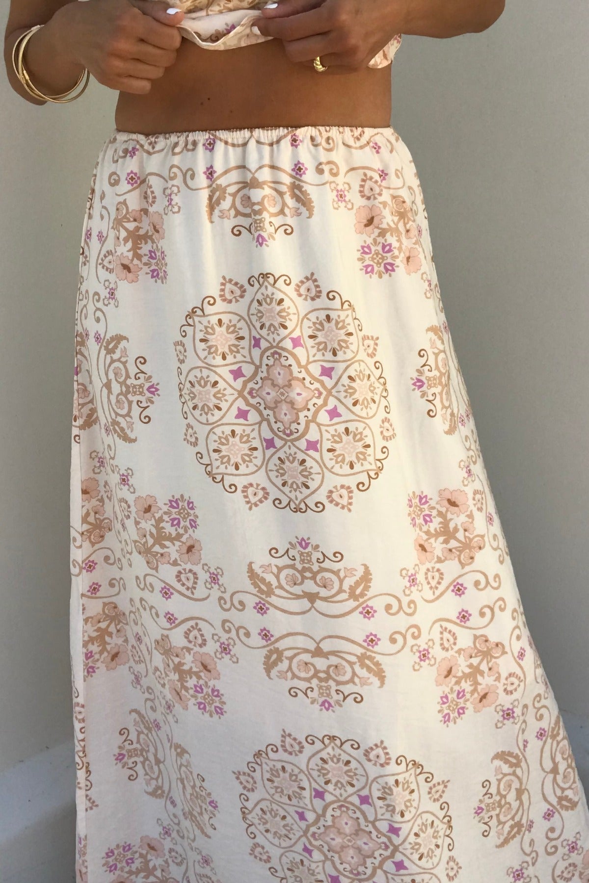 Someone wears the Evelyn Cream Print Maxi Skirt with a pink floral pattern, showing their midriff and gold jewelry.