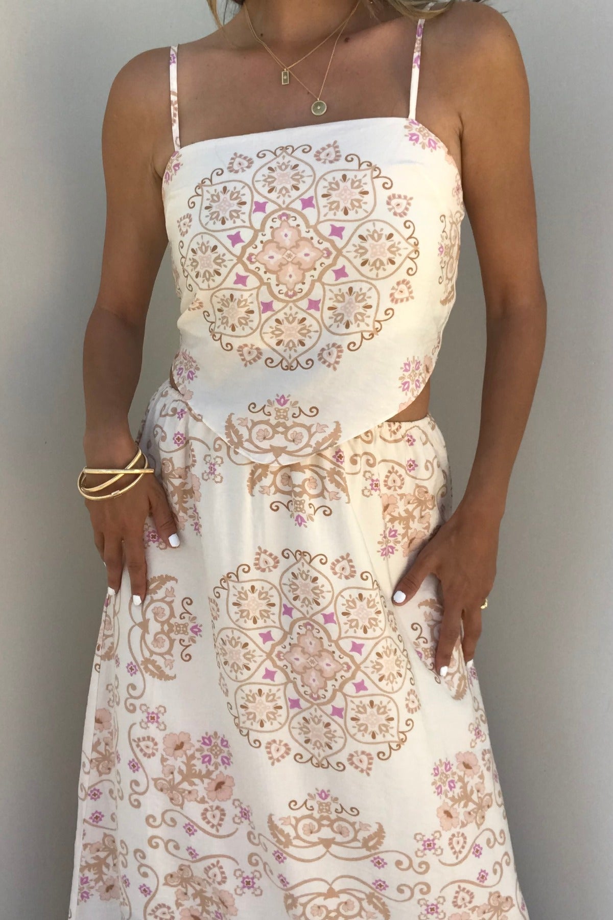 Woman wears the Evelyn Cream Print Tank Top with bandana-inspired patterns, gold jewelry, and white nails against a plain wall.