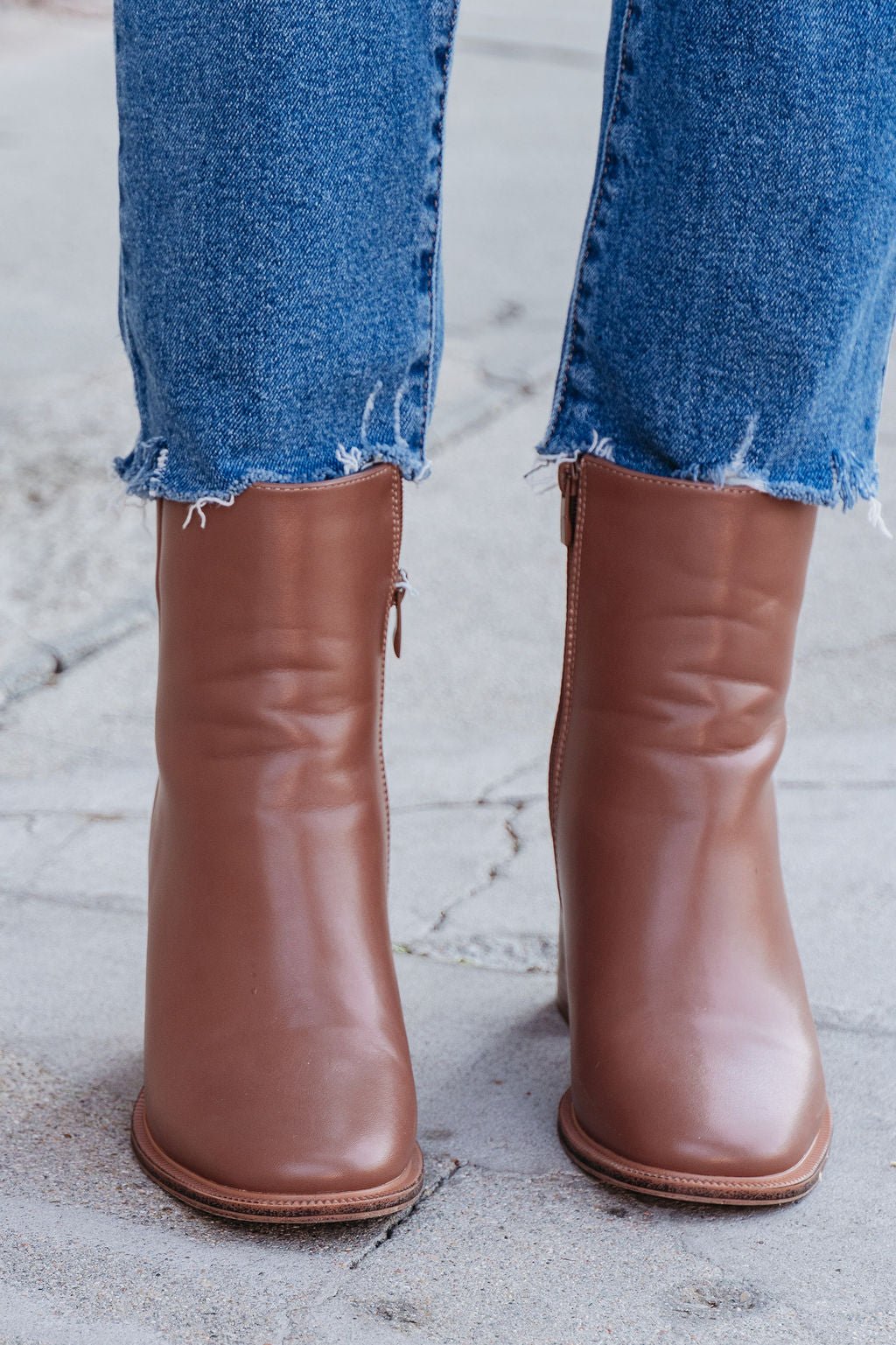 Evelyn Taupe Leather Heeled Ankle Booties paired with frayed hem blue jeans, shown from the front on a concrete surface.