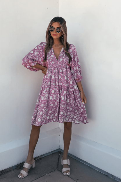 Woman wearing the Everly Pink Floral Print Mini Dress and white sandals, posing by a white wall.