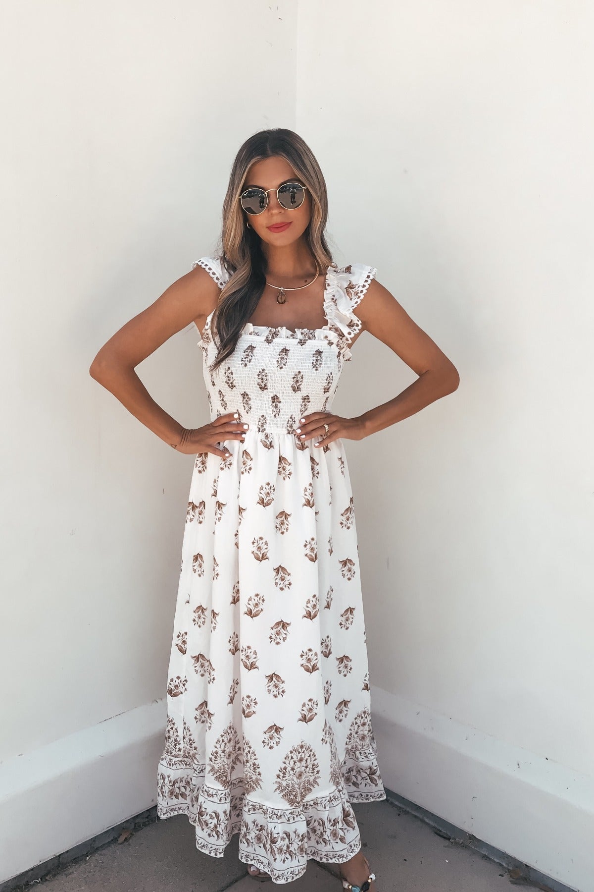 Woman in the Everly Smocked Print Midi Dress - Ivory, with ruffled sleeves, poses in sunglasses against a plain white wall.