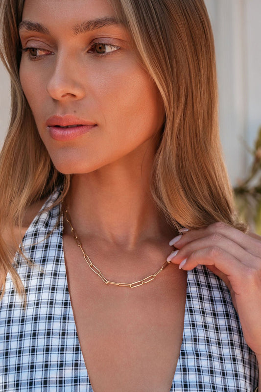 Woman with long hair in a plaid halter top wears the Farrah B Eden Gold Plated Chain Link Necklace, looking to the side.
