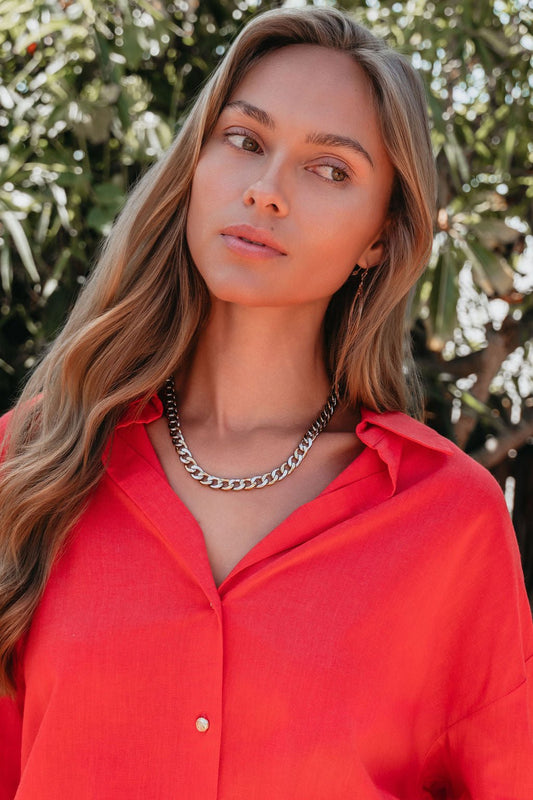 Woman with long wavy hair wears a red shirt and the Farrah B Gold Plated Mixed Metal Chain Necklace, standing outdoors.