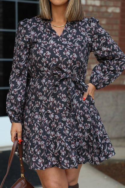 Woman wears a Floral Print Tie Mini Dress in charcoal, standing outdoors and holding a brown handbag.