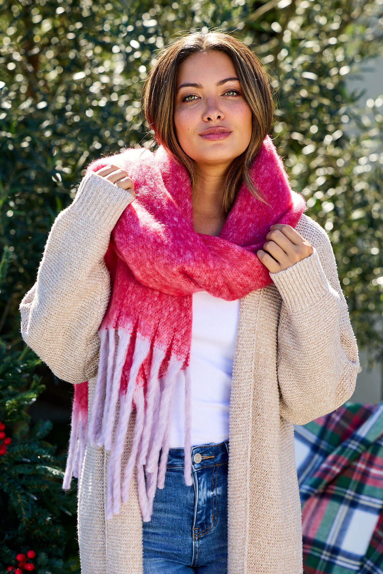 Woman outdoors in a beige cardigan, jeans, and Fluffy Red Ombre Fringe Blanket Scarf—chic winter accessory style by greenery.