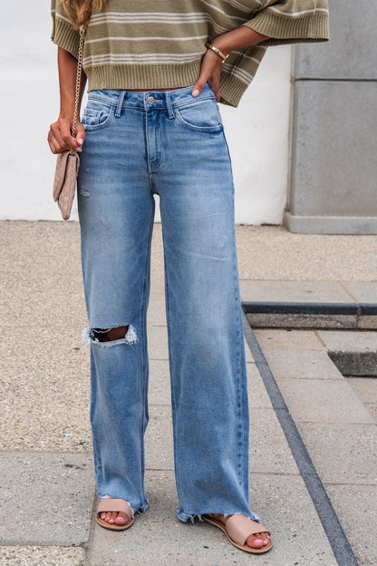 A person wears an olive-striped sweater, Flying Monkey Distressed Raw Hem Jeans - Light Wash, tan sandals, and holds a beige quilted purse.