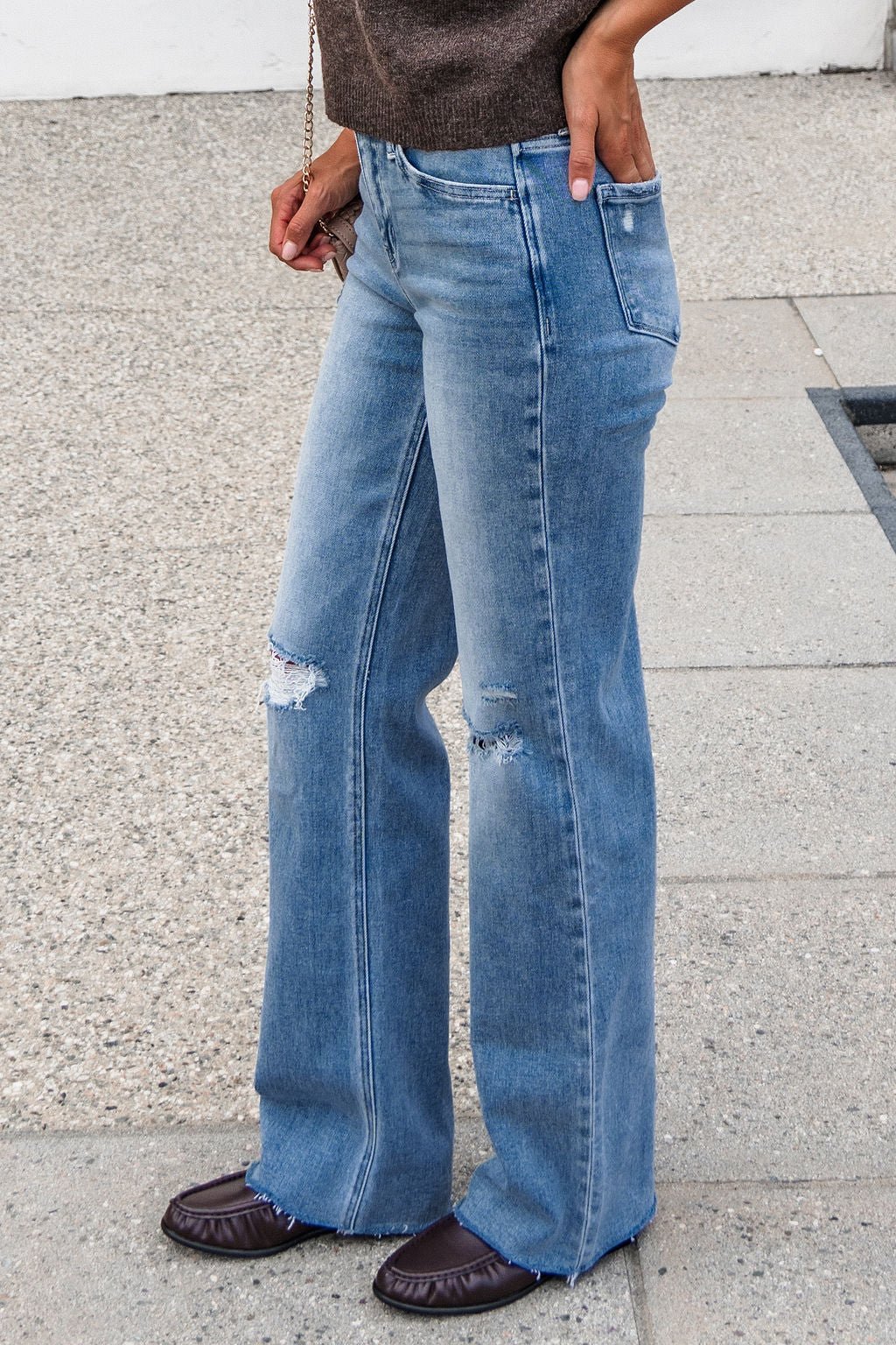 Person in Flying Monkey Distressed Wide Leg Jeans - Light Wash, brown top, and flats stands on textured pavement.