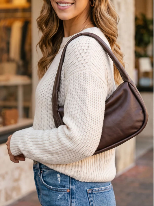 A person in a white sweater carries a dark brown, crescent-shaped leather Free People Alexa Shoulder Bag - Espresso.