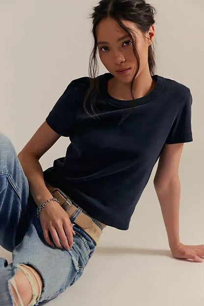 Woman wears the Free People Atlas Crew Tee in charcoal with ripped jeans, seated on the floor, looking at the camera.