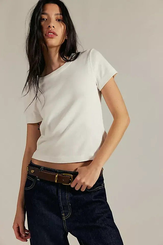 Woman with long dark hair models the Free People Atlas Crew Tee - Ivory with dark jeans, highlighting its fitted shape against a plain backdrop.