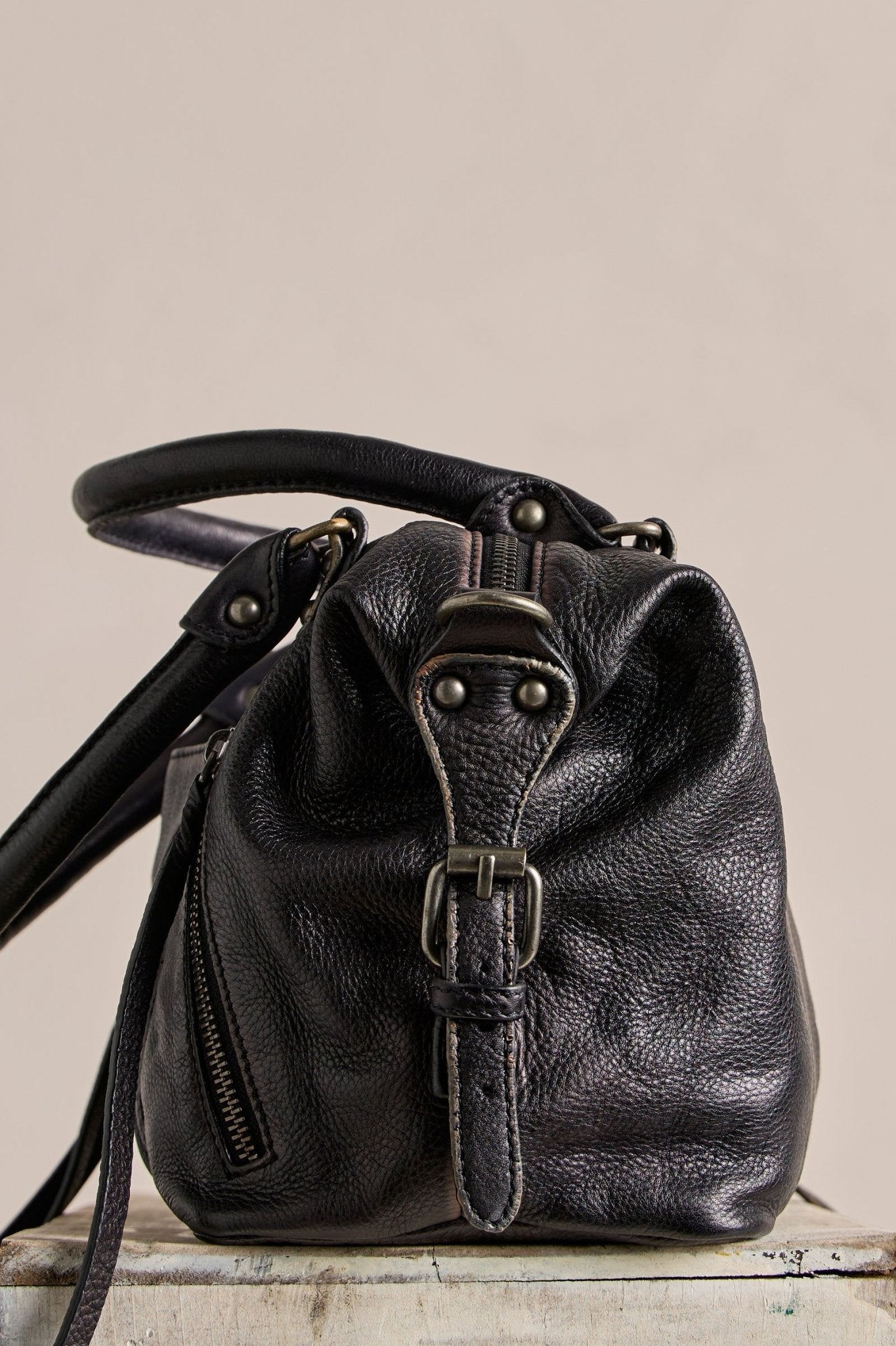 The Free People Baby Emerson Tote Bag in black, with buckle and zipper details, sits on a light-colored surface.