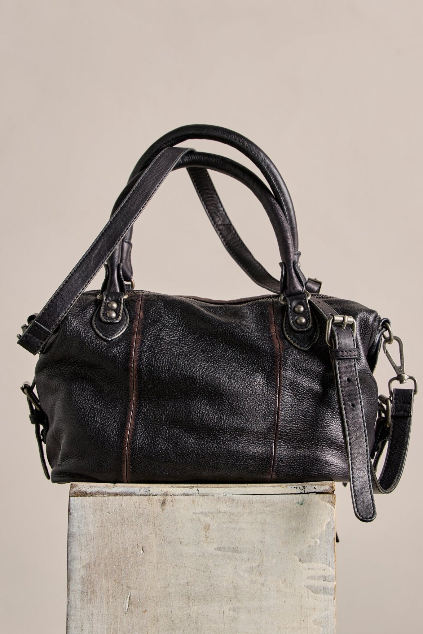 The Free People Baby Emerson Tote Bag in black features dual handles and a detachable strap, shown on a rustic box.