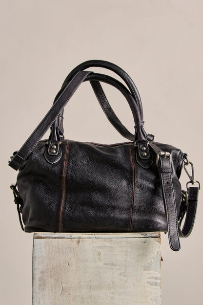 The Free People Baby Emerson Tote Bag in black features dual handles and a detachable strap, shown on a rustic box.