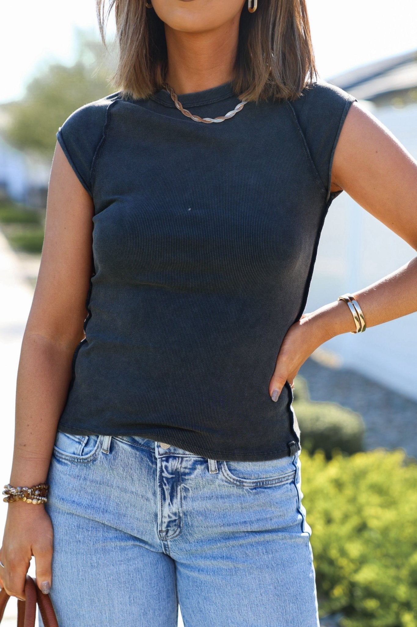 Person wearing a black sleeveless top and blue jeans with a blurred outdoor background