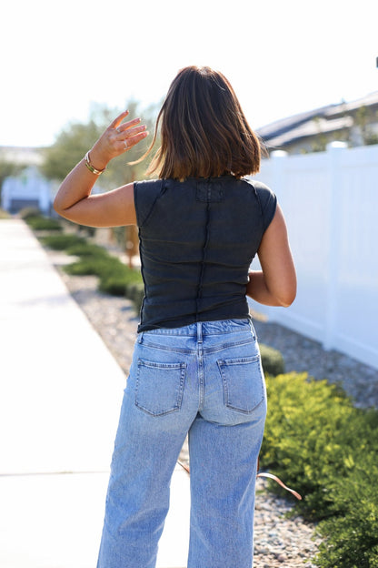 Person wearing a black sleeveless top and light blue jeans walking outdoors.