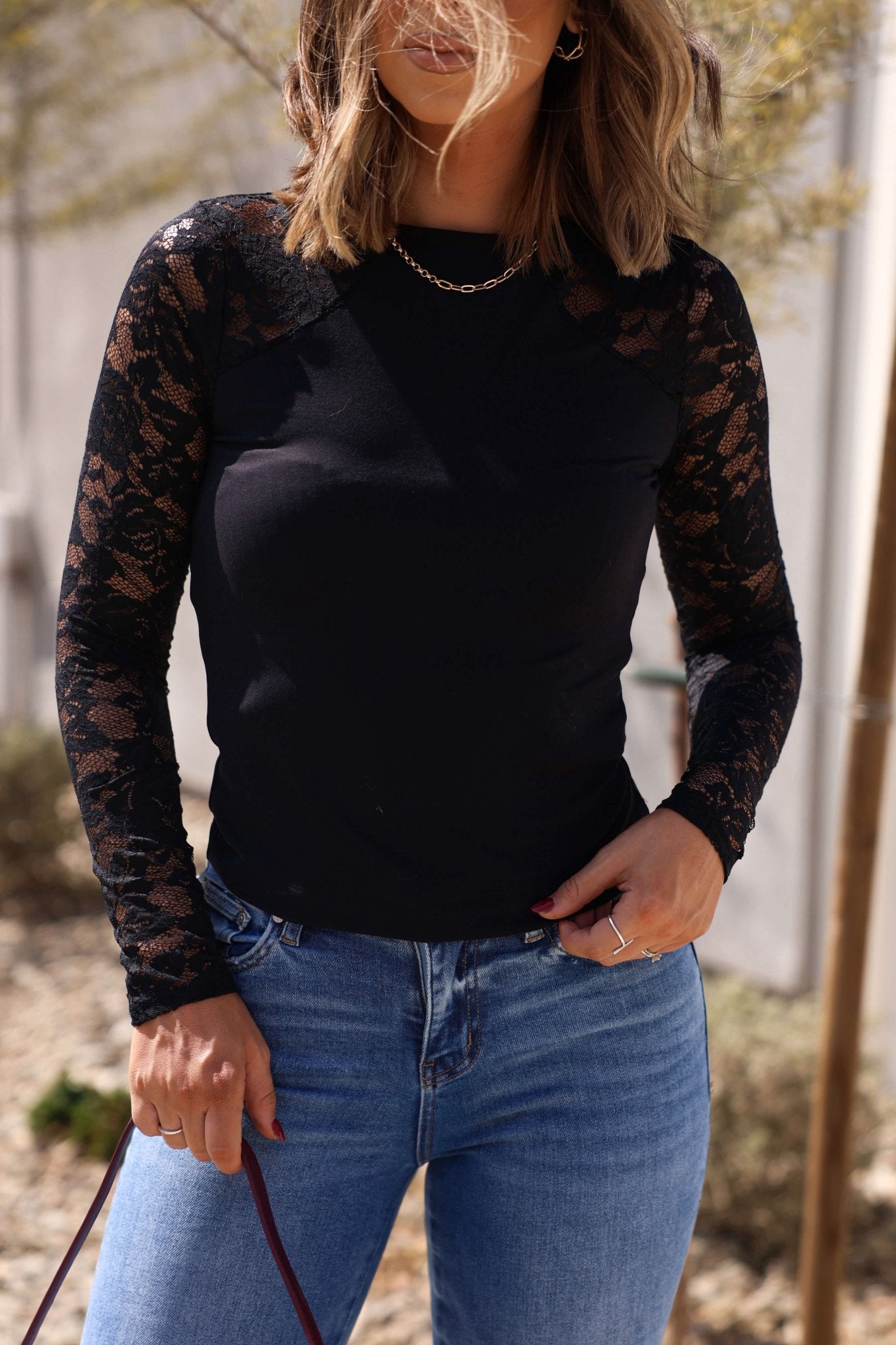 Woman in a Free People Black No Excuses Lace Top - FINAL SALE, sheer sleeves, paired with blue jeans, standing outdoors.