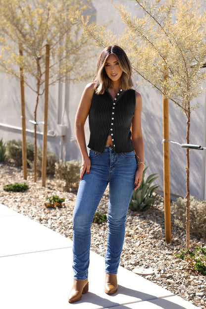 Woman stands outdoors wearing a Free People Black Tilly Vest Top, blue jeans, tan boots, with small trees in the background.