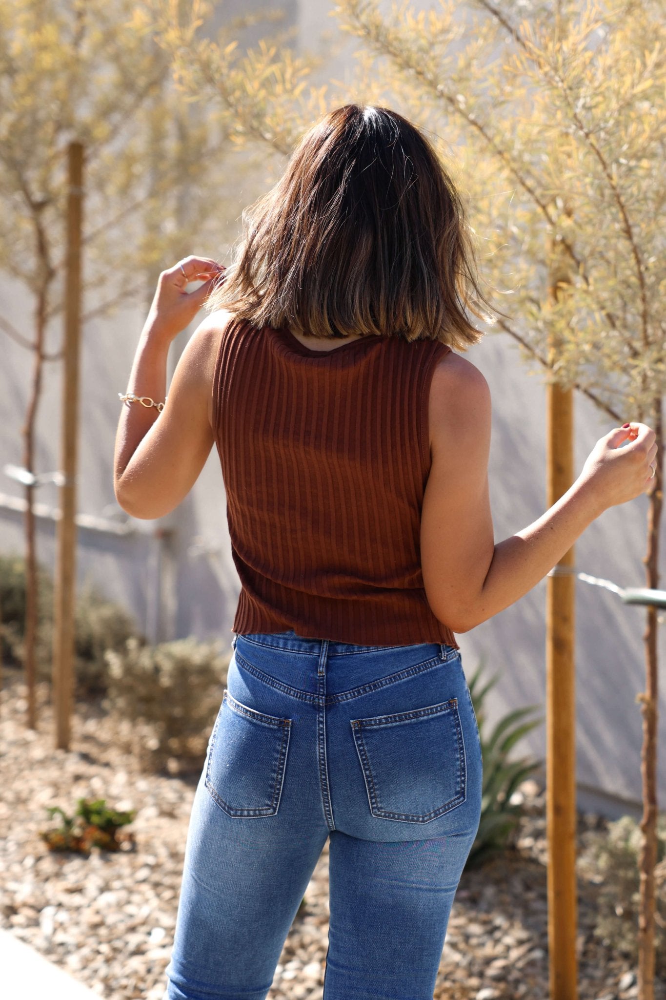 A woman wears the Free People Brown Tilly Vest Top with blue jeans outdoors, her back to the camera.