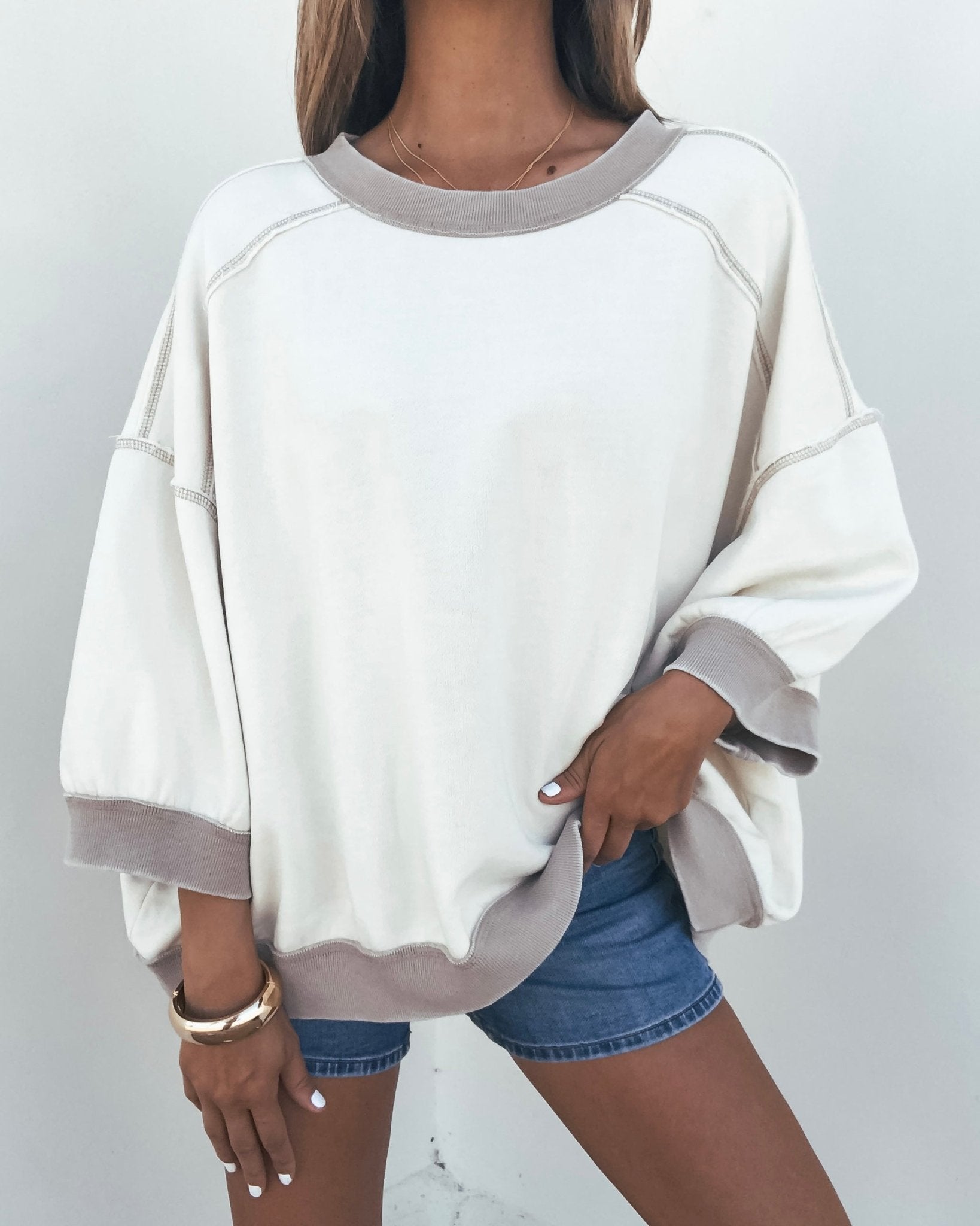 Woman wears Free People Cream Everything Pullover with denim shorts and bracelets, posing against a plain background.