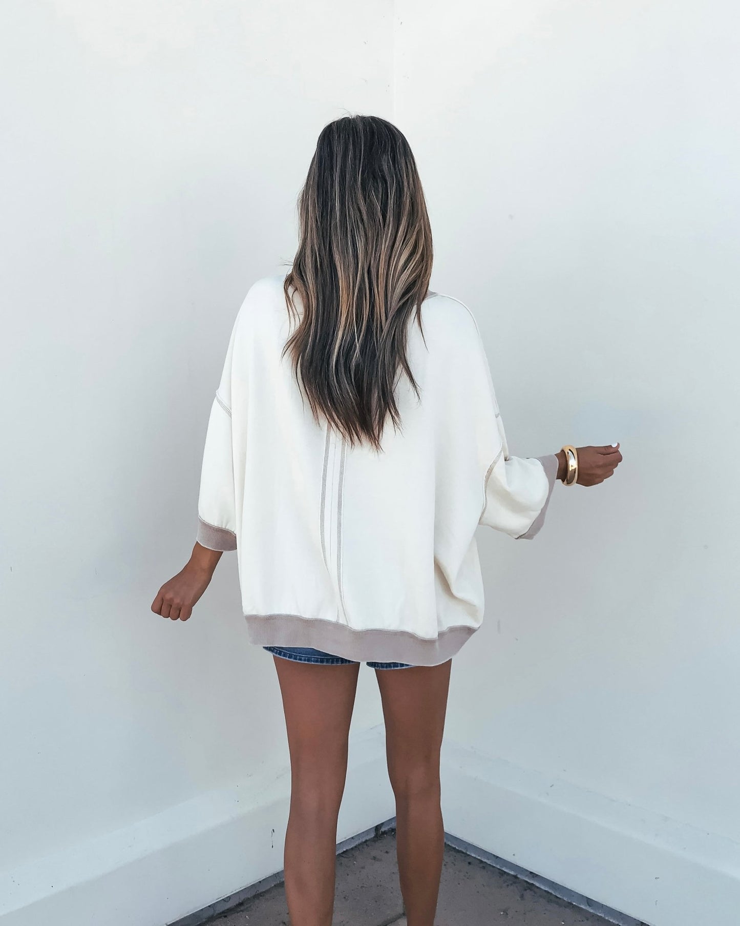 Woman with long hair wears the Free People Cream Everything Pullover, standing with her back to the camera against a white wall.
