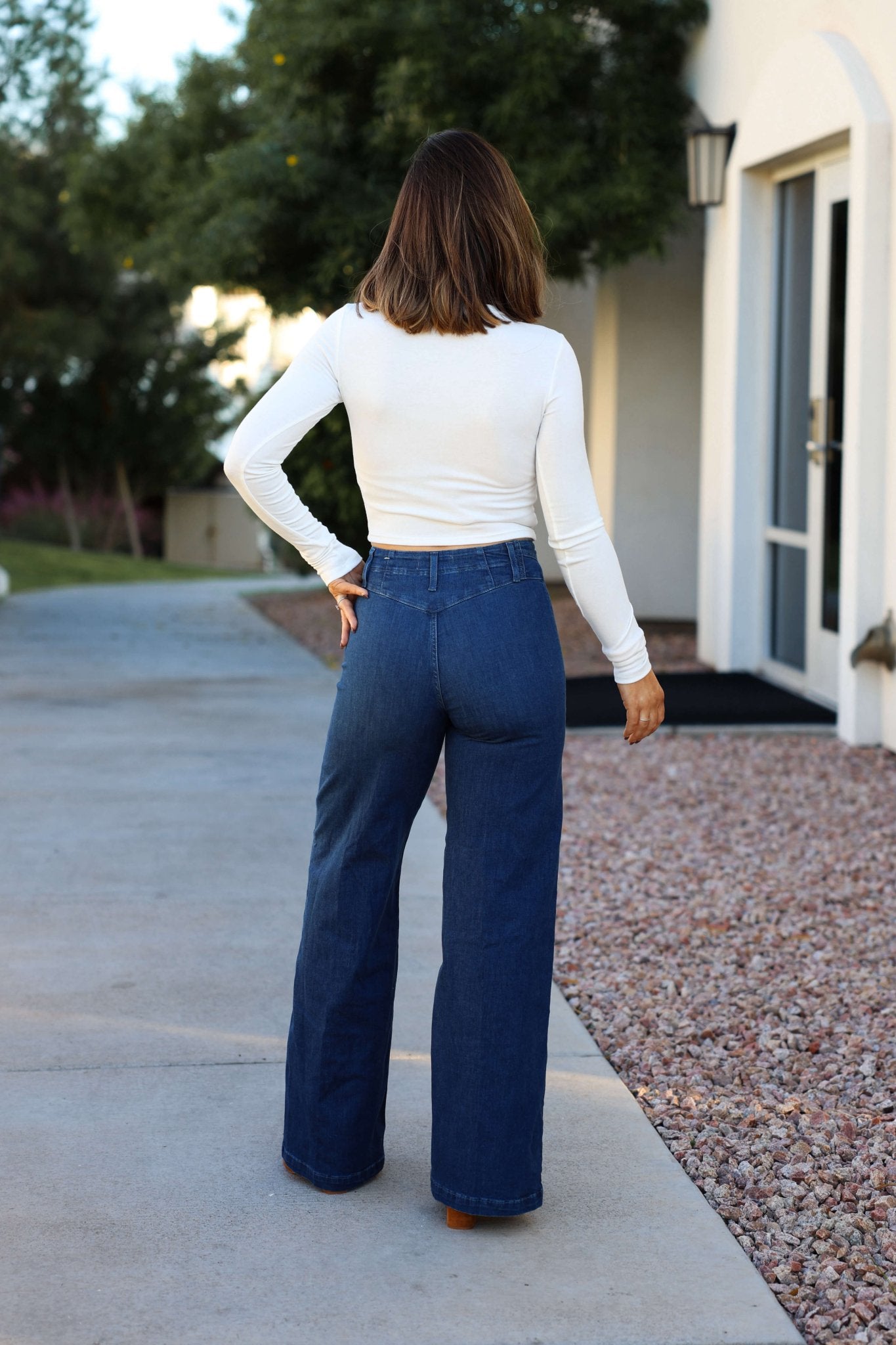 A woman in a white long-sleeve top and Free People Dark Wash Libre Wide Leg Jeans stands outside, facing away.