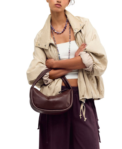 A woman holding a dark brown crescent-shaped FREE PEOPLE ESPRESSO ALEXA SHOULDER BAG.