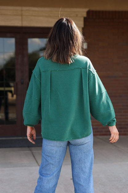 Someone wearing a Free People Forest Green Total Eclipse Tee and blue jeans stands outdoors, facing away from the camera.