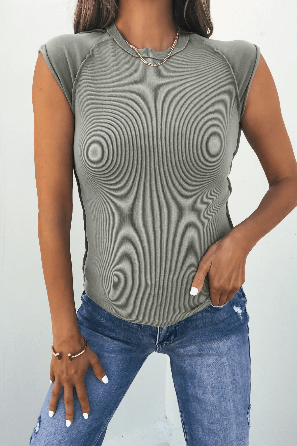 Woman in a Free People Green Ever Had Tee and blue jeans, gold jewelry, posing with one hand on her hip.