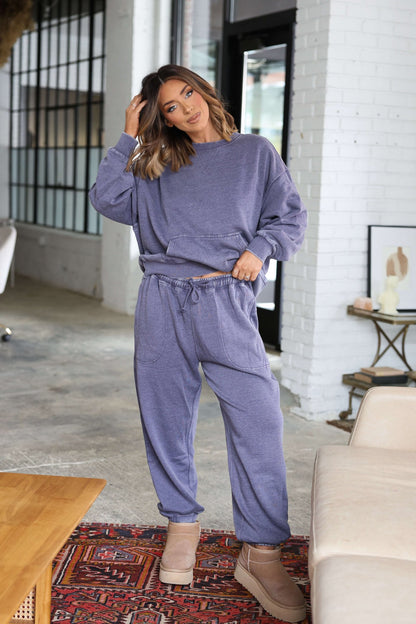Woman in Free People Grey Slow It Down Joggers and beige boots poses indoors by a couch, touching her hair.