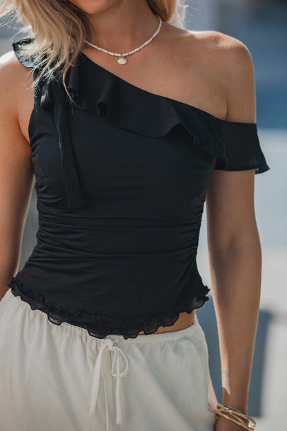 Woman wearing the Free People Isla Off The Shoulder Top in black, styled with white drawstring pants and a necklace outdoors.