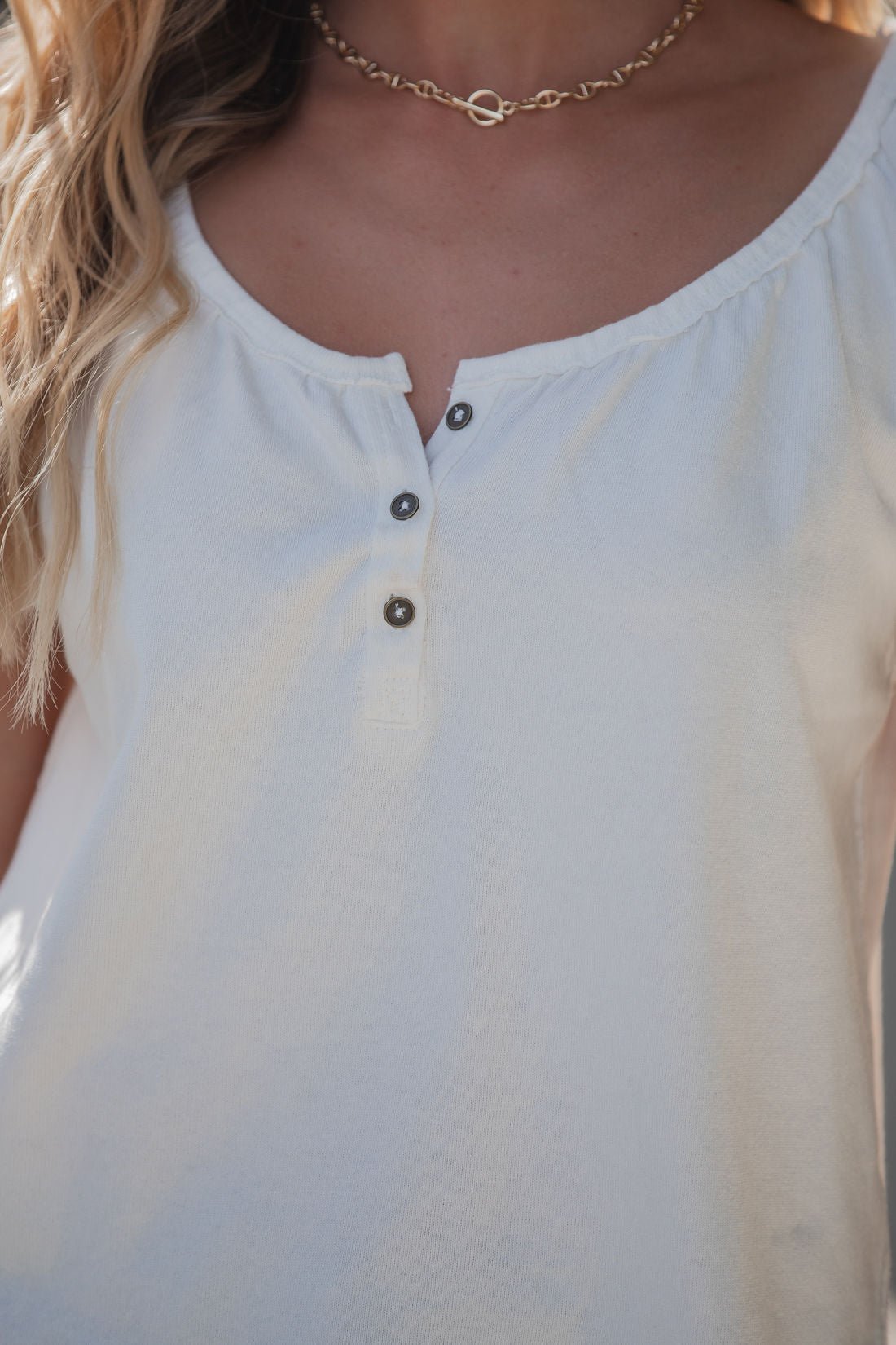 A woman wears the Free People Issa Tee - Ivory, a scoop-neck henley, paired with a gold chain necklace, shown shoulders to chest.