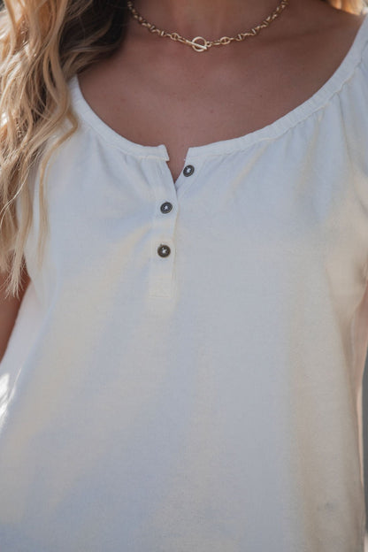 A woman wears the Free People Issa Tee - Ivory, a scoop-neck henley, paired with a gold chain necklace, shown shoulders to chest.