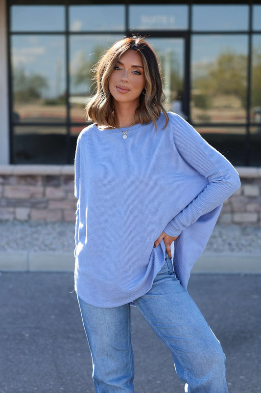 Woman in a Free People Latte Blues Solid Thermal Top and jeans poses outdoors with one hand on her hip by a glass building.