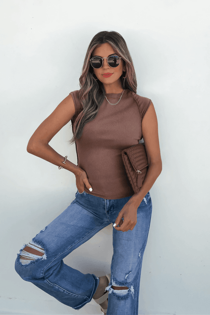 Woman in sunglasses wears the Free People Mocha Ever Had Tee and ripped jeans, holding a brown clutch against a white wall.