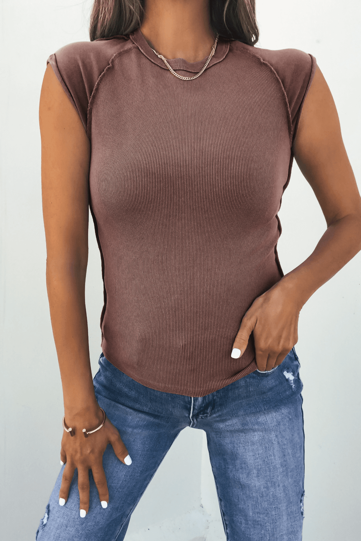 Woman in a Free People Mocha Ever Had Tee, blue jeans, gold necklace and rings, one hand resting on her hip.