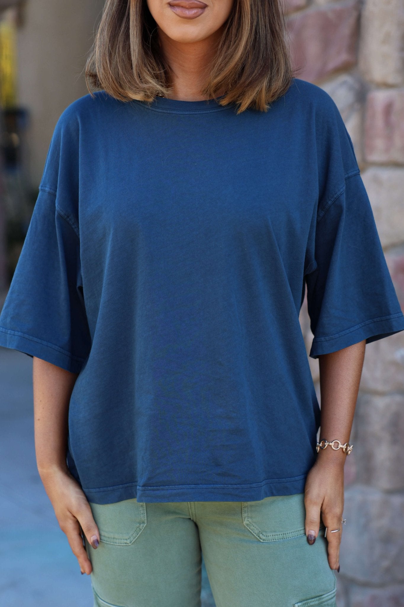 A woman in a Free People Navy Perfect Oversized Tee and green pants stands outside, her face partially out of frame.