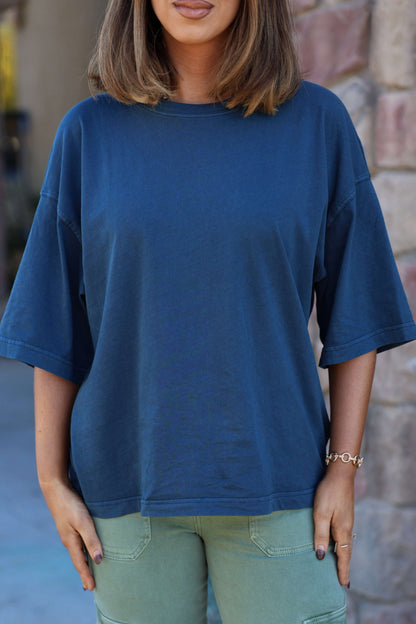 A woman in a Free People Navy Perfect Oversized Tee and green pants stands outside, her face partially out of frame.