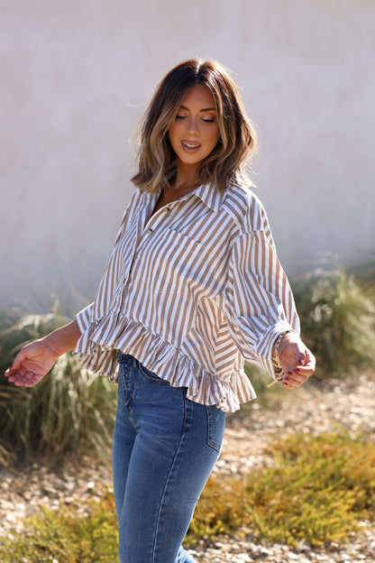 A woman in the Free People Neutral Bailey Stripe Shirt stands outdoors, smiling with greenery in the background.