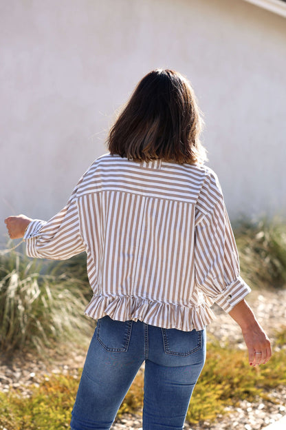 A woman with shoulder-length brown hair wears the Free People Neutral Bailey Stripe Shirt, standing outdoors with her back to the camera.