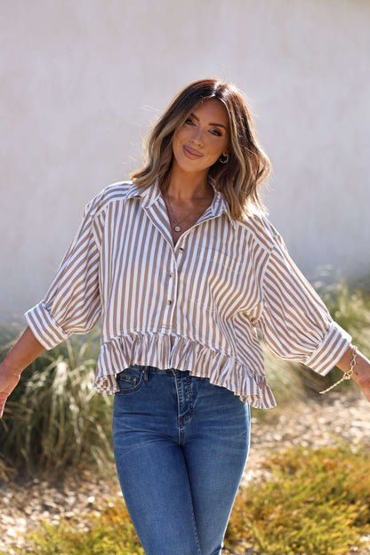 Woman smiling outdoors in the Free People Neutral Bailey Stripe Shirt – FINAL SALE, paired with blue jeans, arms outstretched.
