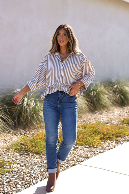 Woman in Free People Neutral Bailey Stripe Shirt, blue jeans, and brown ankle boots walking outdoors on a sunny day.